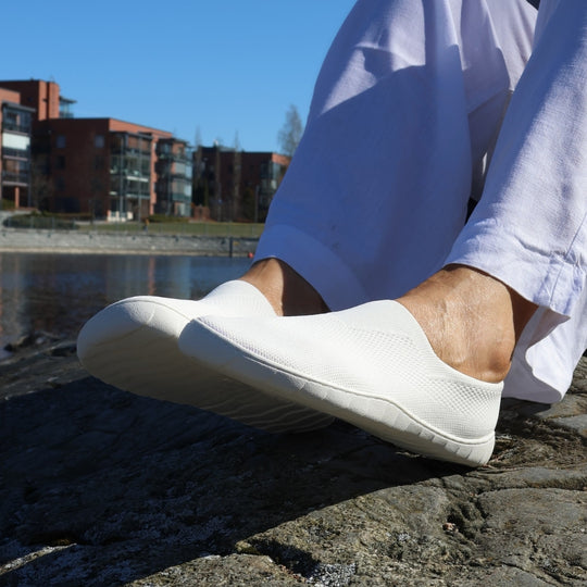 White Vaistoa Lempeä 3 slip-on barefoot shoes worn on feet by the water outdoors