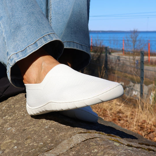 White Vaistoa Lempeä 3 slip-on barefoot shoes worn on feet in side view outdoors by the water