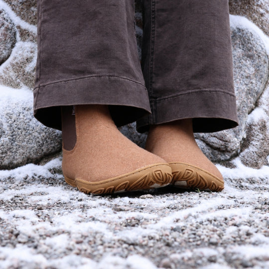 Vaistoa Sulo 2 barfota chelsea-boots för vinter – livsstilsbild: paret framifrån på en snöig klippa med mörkbruna byxor, den elastiska resåren syns