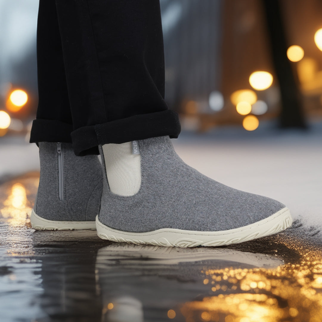 Pearl grey barefoot winter felt Chelsea boots worn with black pants in a snowy winter environment, shown from the side to highlight their natural foot shape, flexibility, and elegant design.