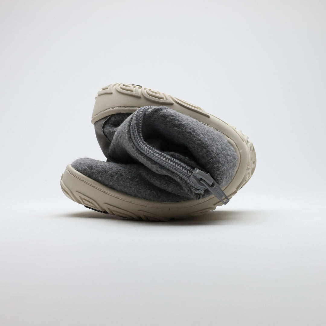 Pearl grey barefoot winter felt Chelsea boot folded to demonstrate its thin and flexible sole on a light gray background.