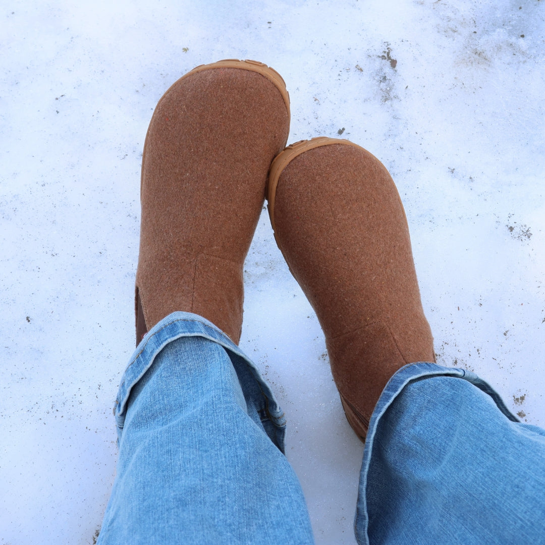 Roasted almond barefoot winter felt Chelsea boots worn with blue jeans in a snowy winter scene, shown from above to highlight the wide anatomical toe box and natural foot shape.