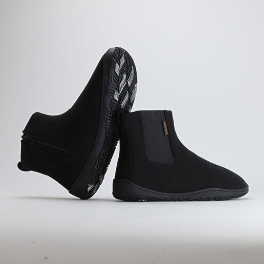 Kaksi samettisen mustaa Vaistoa Sulo -huopanilkkuria nojaavat toisiinsa siten, että kengän pohjan kuviointi ja kitkapalat näkyvät selkeästi. Kuva tuo esiin Vaistoa Pitoa™ -talvipohjan pitävän ja kevyen rakenteen.