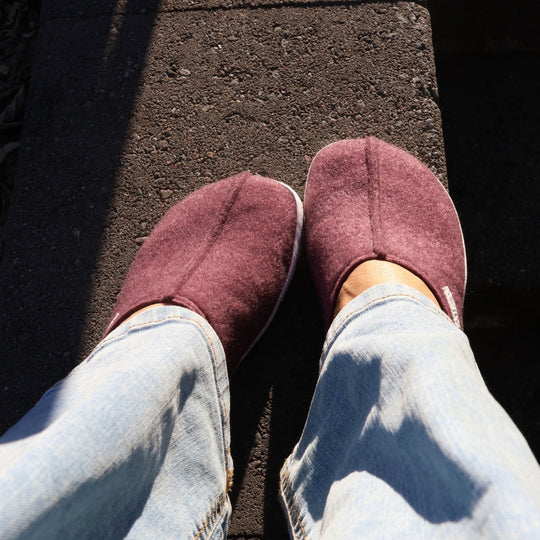Vaistoa Toive felt barefoot slippers – burgundy felt slippers worn and shown from above, light jeans and strong sunlight on a concrete outdoor step