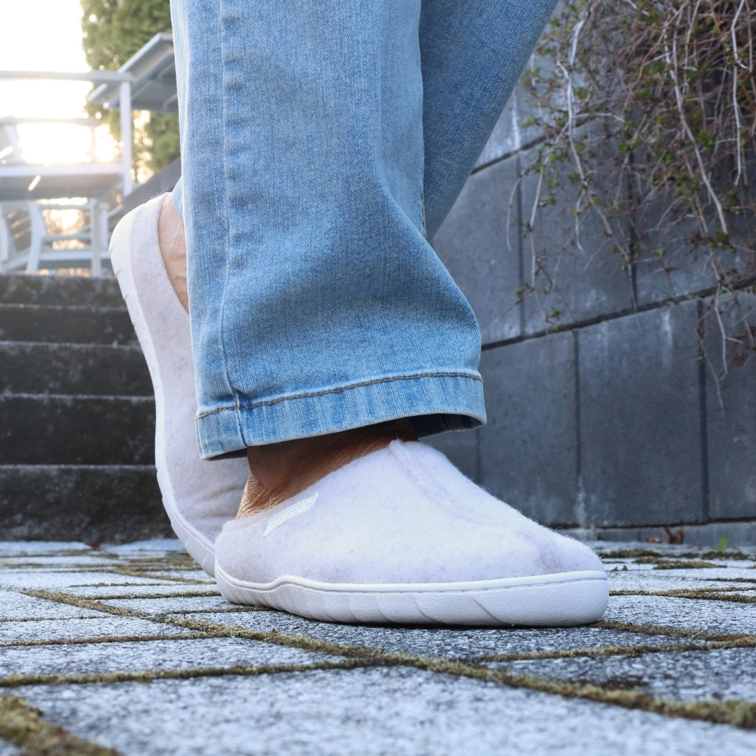 Vaistoa Toive felt barefoot slippers – vanilla grey felt slippers worn outdoors on stone stairs, light blue jeans and low sunlight beside a grey stone wall