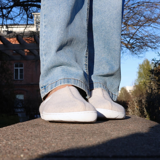 Vaistoa Toive felt barefoot slippers – vanilla grey felt slippers worn outdoors on a stone edge, light jeans and a sunny spring yard surrounded by buildings and trees