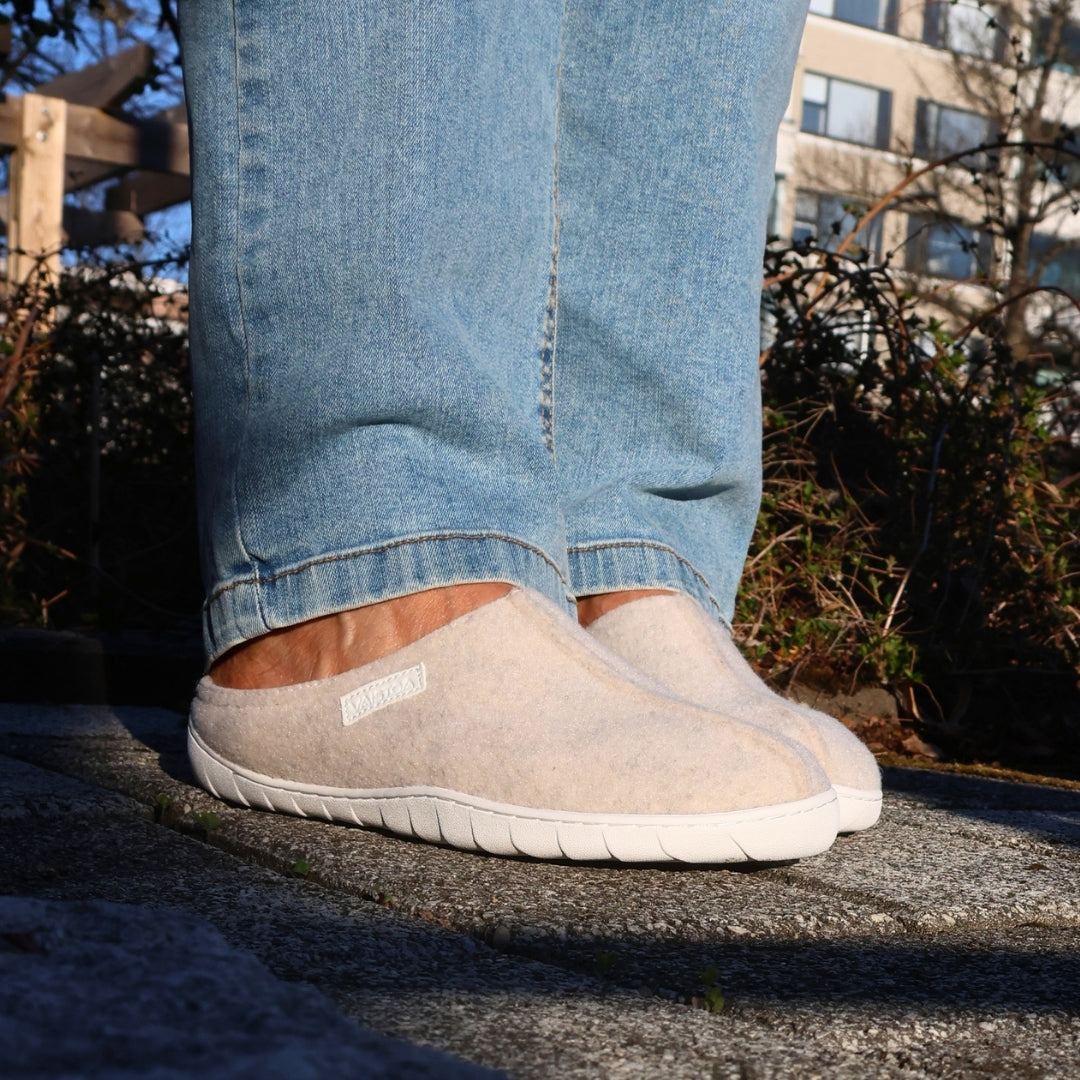 Vaistoa Toive felt barefoot slippers – vanilla grey felt slippers worn outdoors on a stone edge, light jeans and a sunny yard with green plants in the background