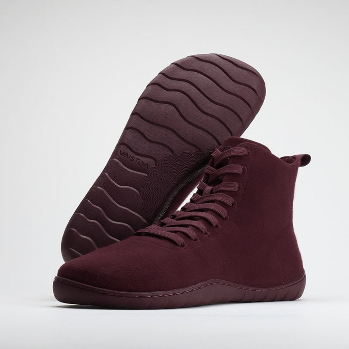 Vaistoa Tunto 2 felt barefoot sneakers – studio shot of the pair with the rear shoe tilted on its side so the outsole faces the camera, showing the wavy tread and the embossed VAISTOA logo, the front shoe seen from a front three-quarter angle with laces and heel loop, burgundy colour