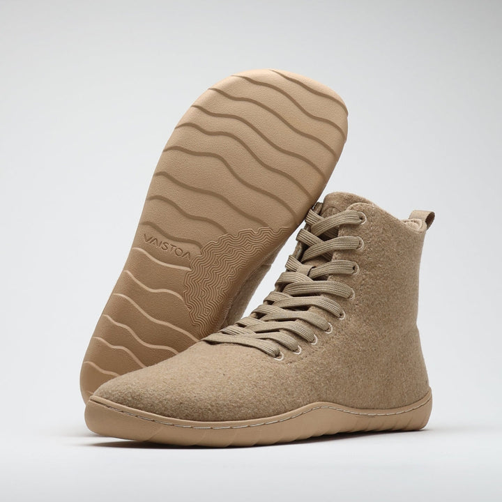 Vaistoa Tunto 2 felt barefoot sneakers – one shoe stands at a front three-quarter angle while the other is propped behind it with the sole facing the camera, revealing the wavy outsole tread, the contour-line pattern under the arch and the embossed VAISTOA logo, sand colour