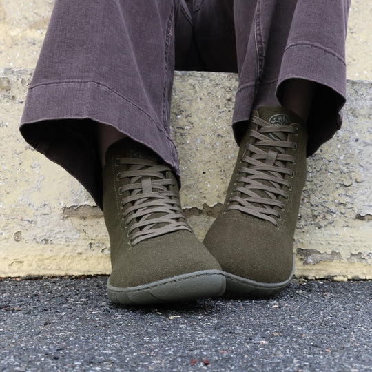 Vaistoa Tunto 2 felt barefoot sneakers – on-foot, dark trousers, seated on a concrete ledge against a yellow wall, front view, olive colour