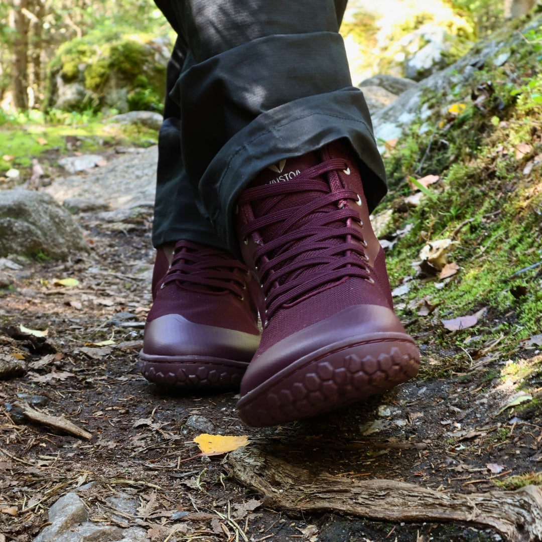 Vaistoa Tuohi 2 barefoot light hiking shoes burgundy – close-up of the shoes being worn, seen from the front mid-stride, with the honeycomb pattern on the leading shoe's outsole visible
