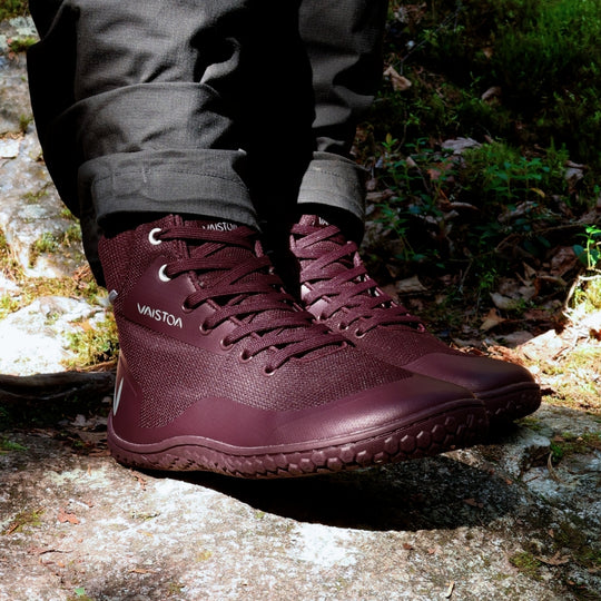 Vaistoa Tuohi 2 barefoot light hiking shoes burgundy – close-up of the shoes being worn, the wearer standing on a rock covered in pale crustose lichen, with moss around it