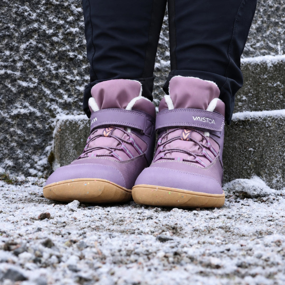 Vaistoa Ulappa 2 kids waterproof barefoot sneakers – lifestyle photo: pair from the front standing on frosty stone steps with black trousers, the Vaistoa logo on the hook-and-loop strap, quick lacing and faux fur lining visible