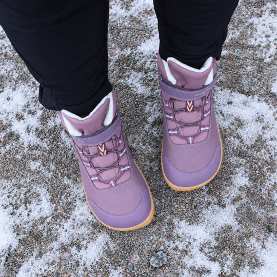 Vaistoa Ulappa 2 kids waterproof barefoot sneakers – lifestyle photo: pair from above standing on frosty asphalt with black trousers, the hook-and-loop strap, quick lacing and faux fur lining visible