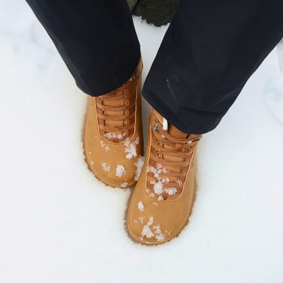 Vaistoa Uoma 4 winter barefoot trekking boots – lifestyle photo: pair from above standing in snow with black trousers, snowflakes on the shoes