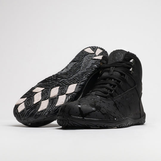 Vaistoa Uoma 4 winter barefoot trekking boots – pair with water droplets on the surface, one shoe lying with the outsole and grip pads facing the camera and the other standing in front of it
