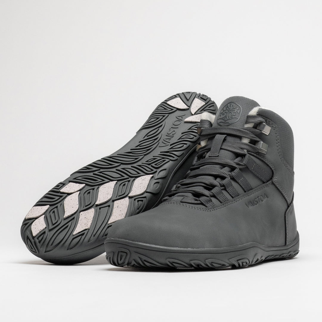 Vaistoa Uoma 4 winter barefoot trekking boots – pair with one shoe lying with the outsole facing the camera showing the light grip pads and the other standing in front of it at a front angle, against a light background